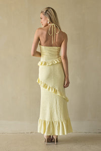 Woman wearing a yellow strapless dress with ruffled details against a beige background