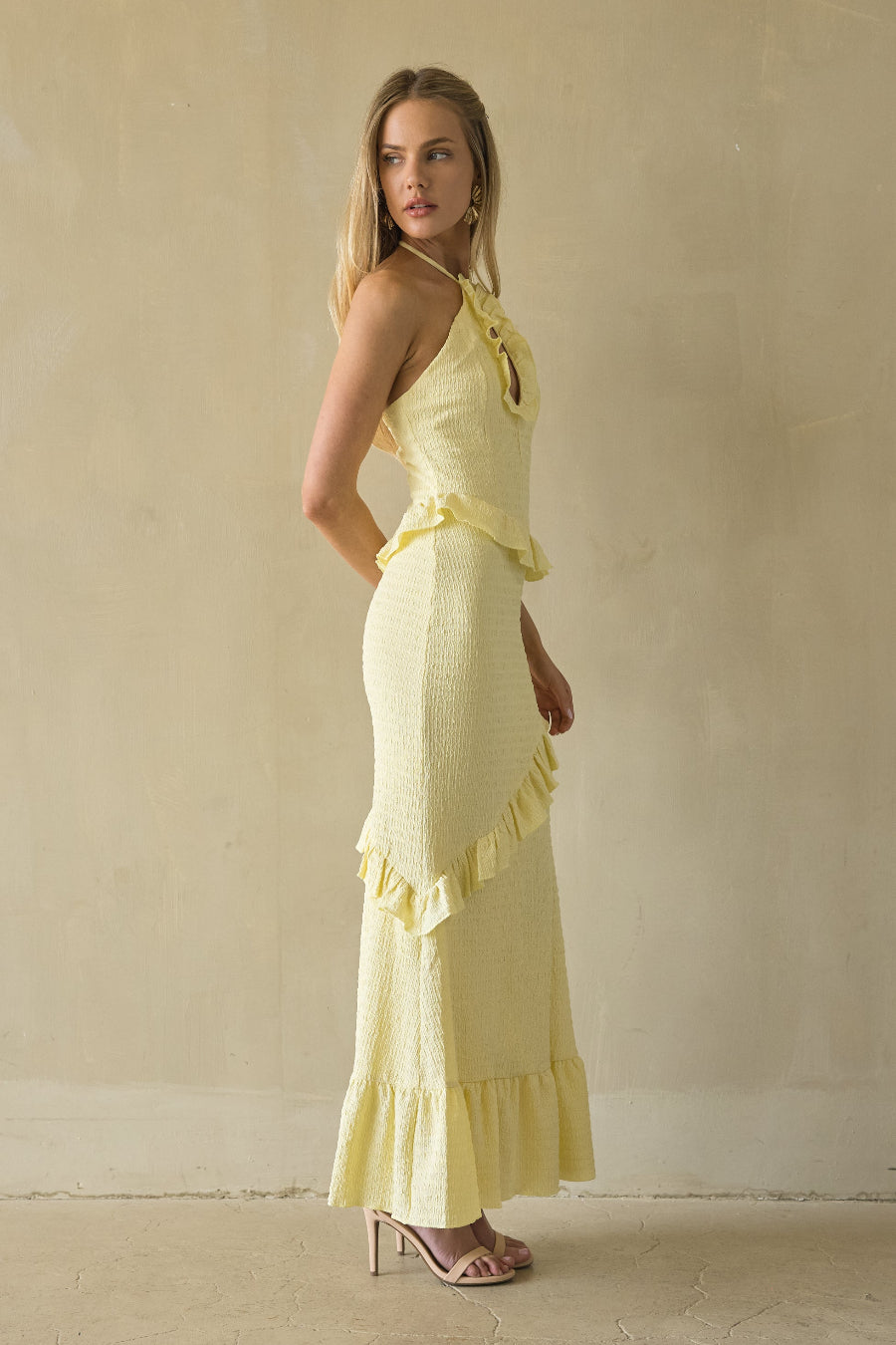 Woman wearing a yellow dress with ruffled details against a beige wall.