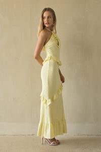 Woman wearing a yellow dress with ruffled details against a beige wall.