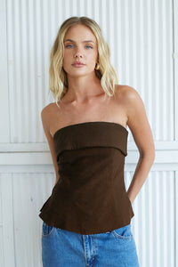 brown-image | Woman wearing a brown strapless top and blue jeans against a white wall.