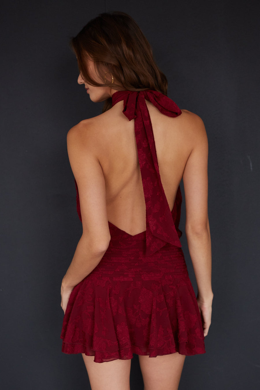 Woman wearing a burgundy dress with a backless design against a dark background