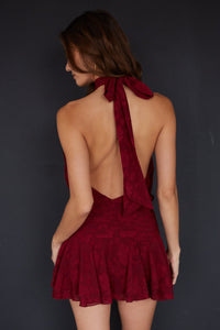 Woman wearing a burgundy dress with a backless design against a dark background
