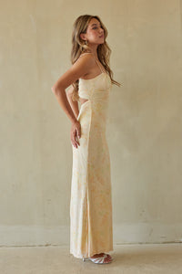 Woman wearing a long, light-colored dress against a plain wall.