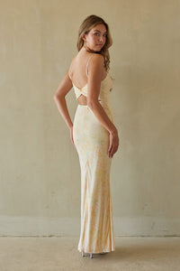 Woman wearing a long, light-colored dress with cut-out design against a plain wall.