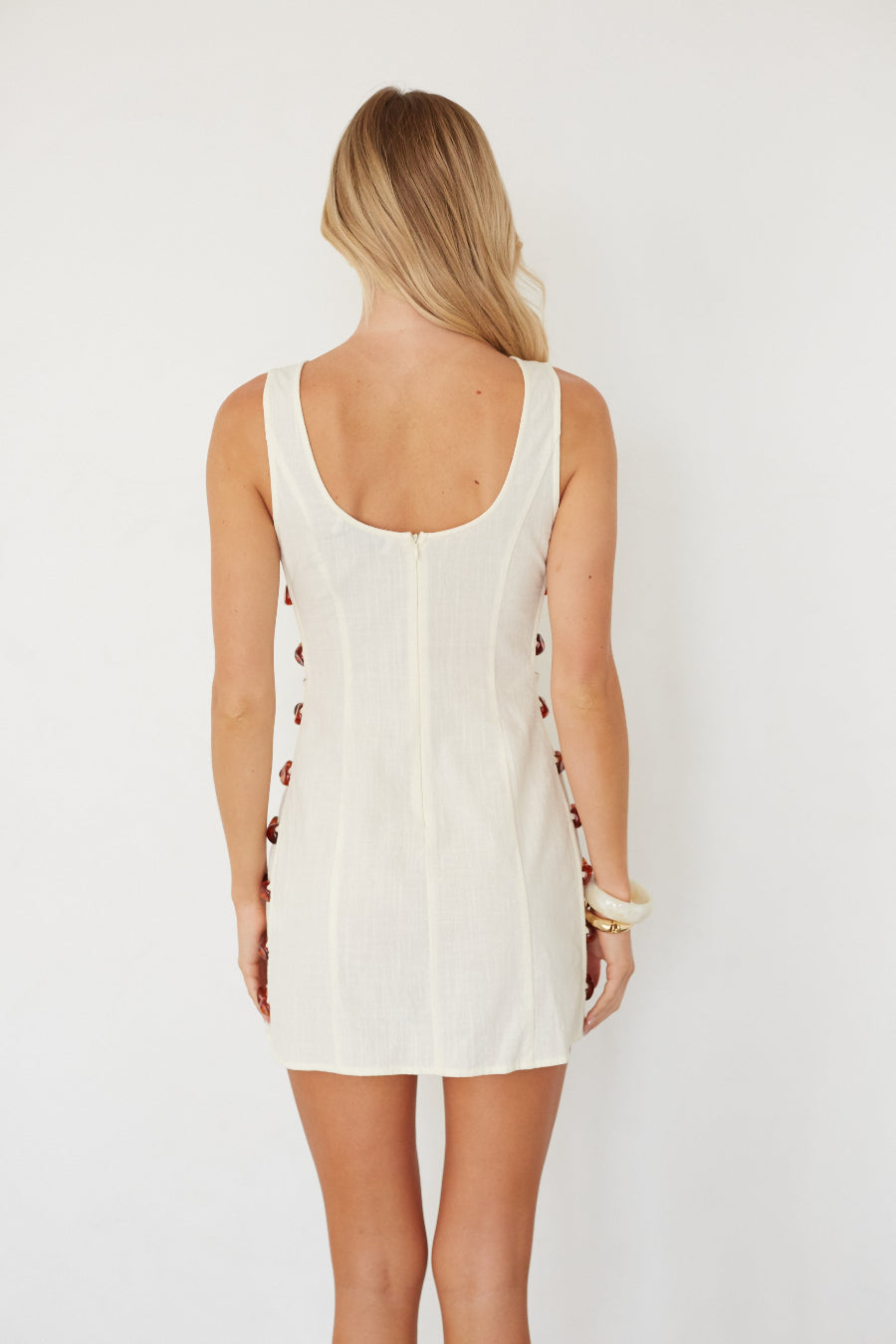 Woman wearing a white sleeveless dress with cut-out details on a plain background