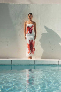 Woman in a floral dress standing by a pool with a neutral background