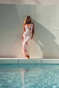 Woman in a white dress standing by a pool with a light blue wall in the background