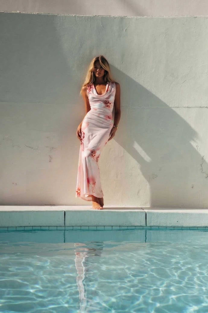 Woman in a white dress standing by a pool with a light blue wall in the background