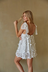 back view of blonde model wearing a white butterfly mini dress with bow straps - unique bridal shower dress