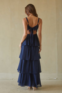 Woman wearing a navy blue dress with a tiered skirt and open back against a plain background