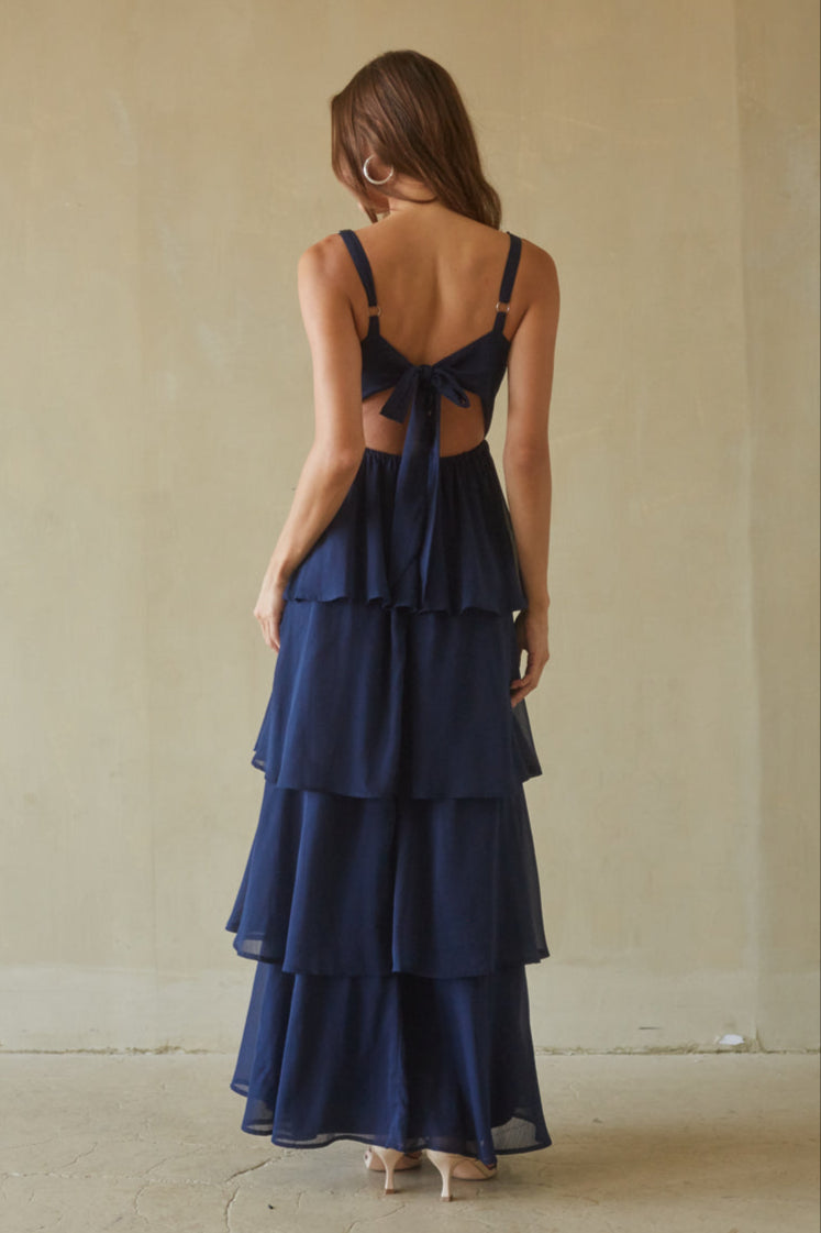 Woman wearing a navy blue dress with a tiered skirt and open back against a plain background