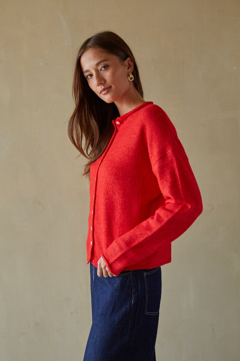 Woman wearing a red shirt and blue jeans against a beige background