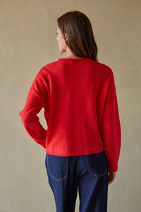 Person wearing a red sweater and blue jeans against a beige background