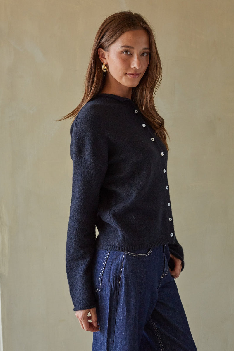 Woman wearing a dark blue sweater with white buttons against a beige background