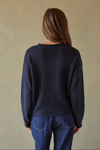 Person wearing a navy sweater and blue jeans against a beige background