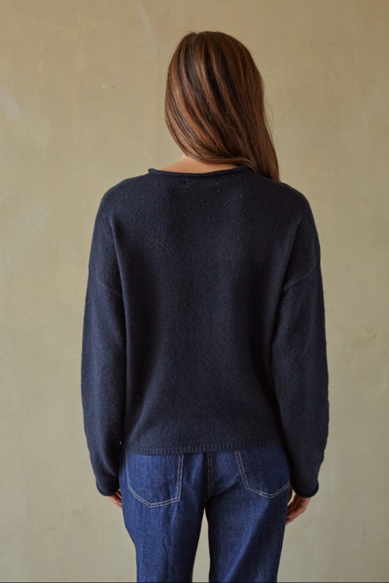 Person wearing a navy sweater and blue jeans against a beige background