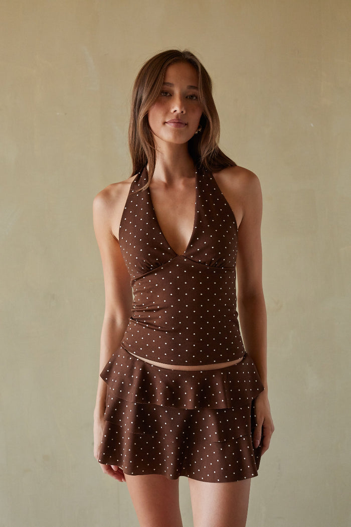 Woman wearing a brown polka dot top and dress against a beige background