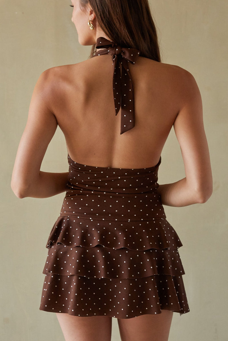 Woman wearing a brown polka dot top with a ruffled skirt against a beige background