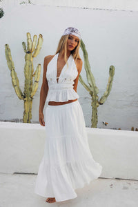 Woman in a white dress standing in front of a cactus plant against a white wall.