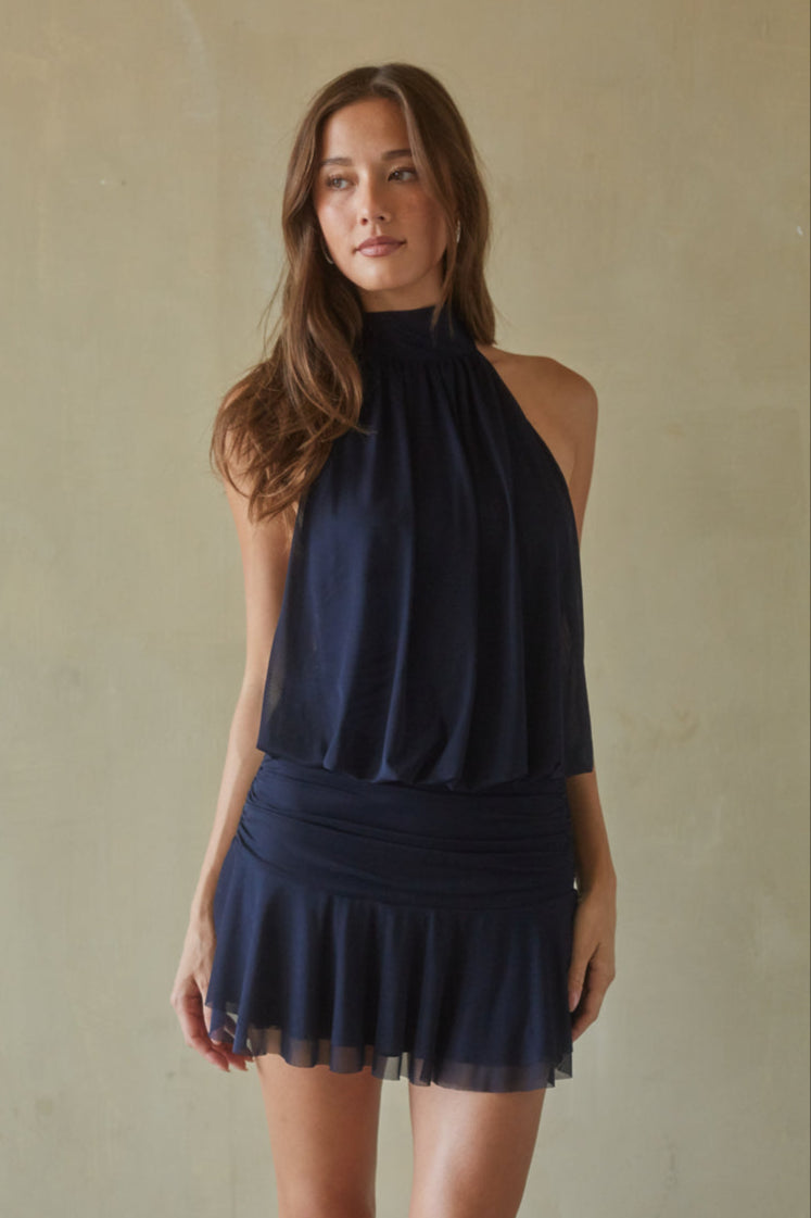 Woman wearing a navy blue halter neck dress against a beige background