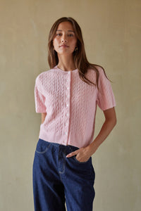 Woman wearing a pink textured blouse and blue pants against a beige background