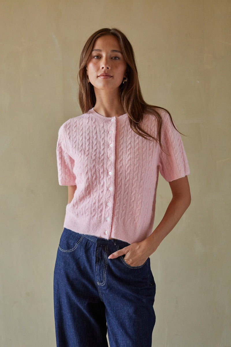 Woman wearing a pink textured blouse and blue pants against a beige background