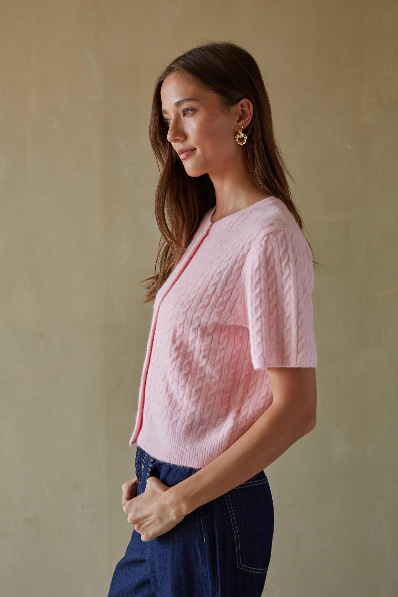 Woman wearing a pink textured top and blue pants against a beige wall