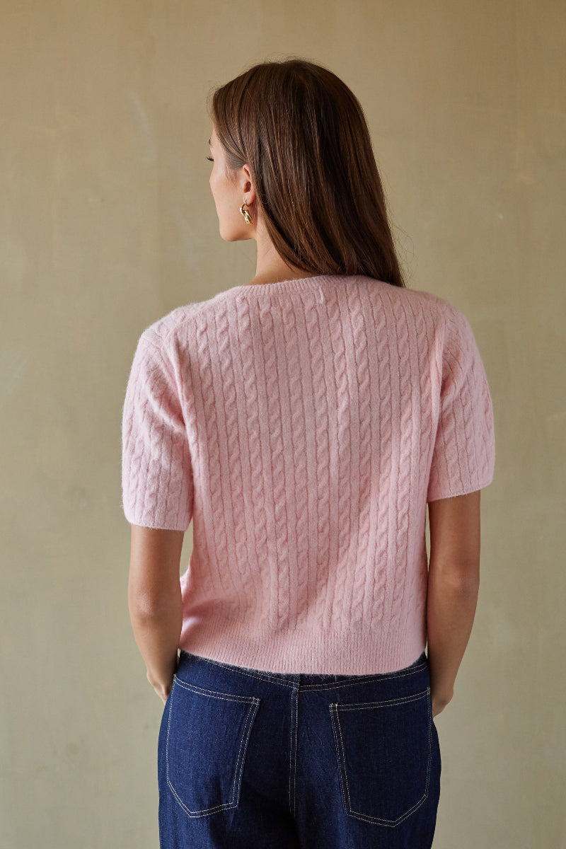 Woman wearing a pink cable knit sweater against a beige background