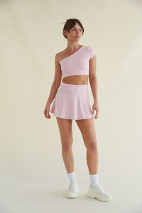 front view studio image with seamless background - female model wearing a one shoulder pink athletic crop top and a matching flare mini skort - wearing crew socks and white chunky steve madden sneakers - women's athleisure - Sunday skin