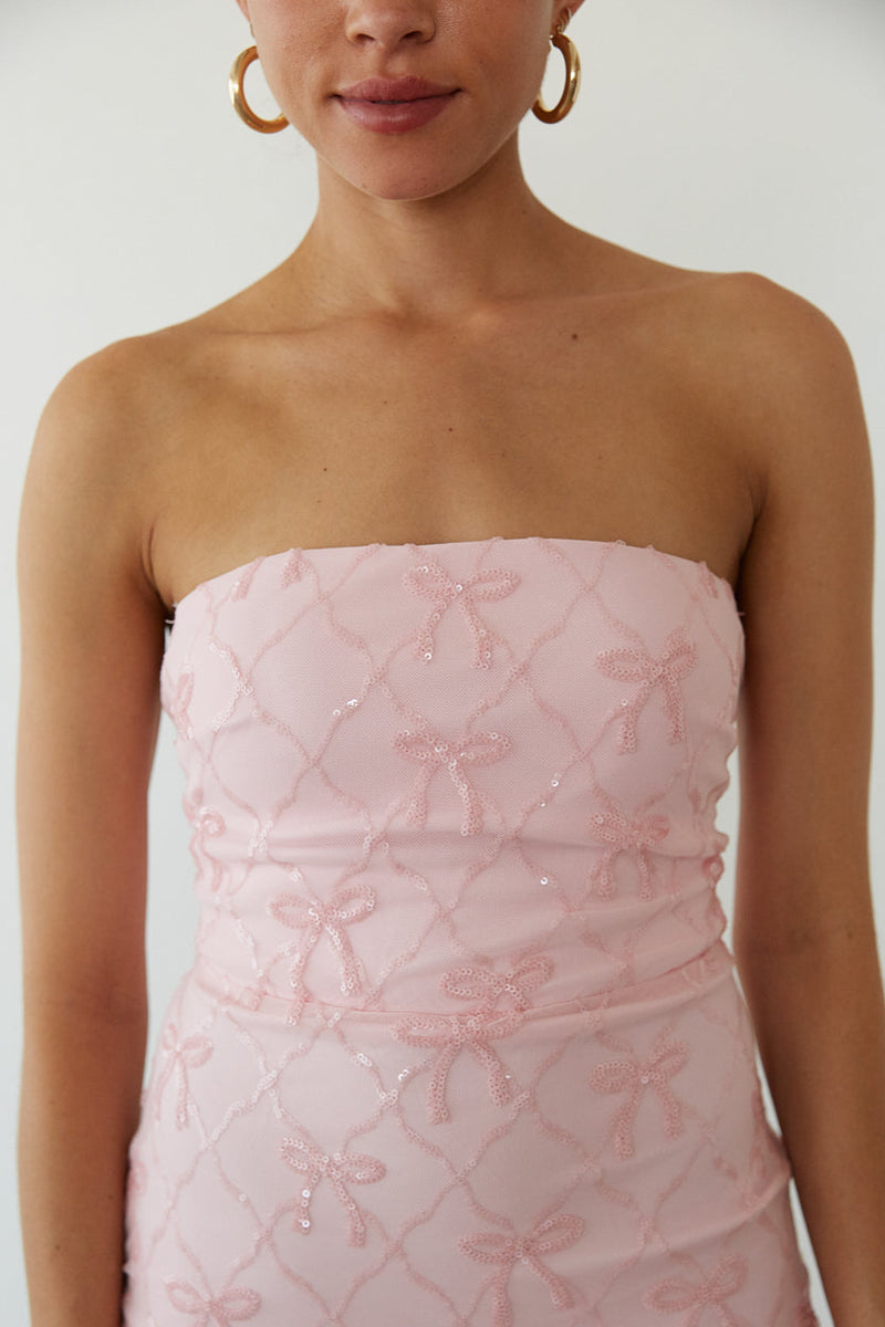 Woman wearing a pink strapless dress with floral patterns on a plain background