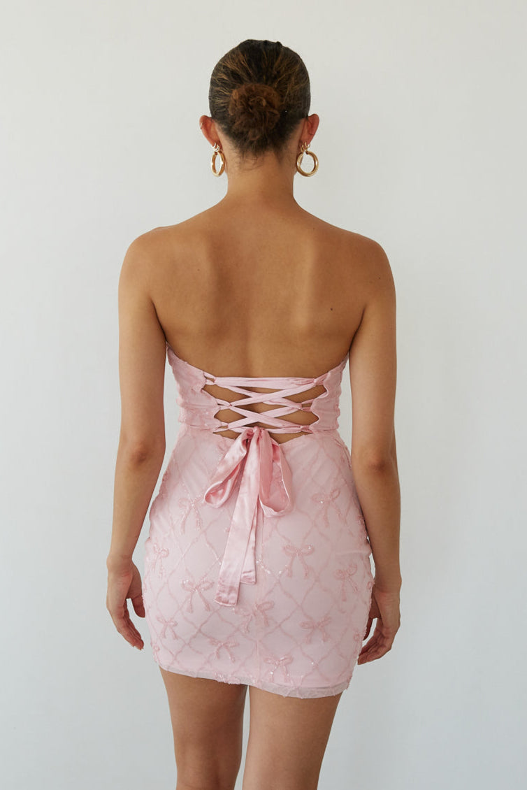 Woman wearing a pink strapless dress with lace-up back on a white background