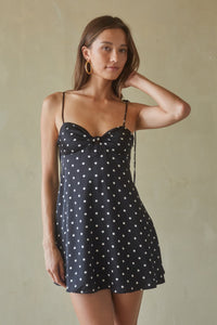 Woman wearing a black polka dot dress against a beige background