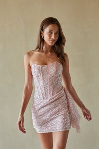 Woman wearing a strapless, light pink sequin dress against a beige background