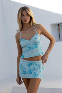 Woman wearing a light blue floral dress against a white wall.