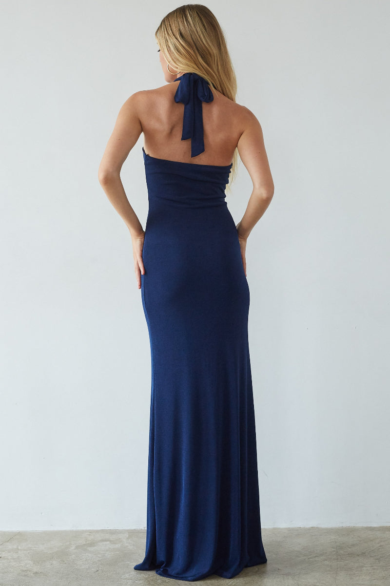 Woman wearing a navy blue halter neck gown with a bow detail on a plain background