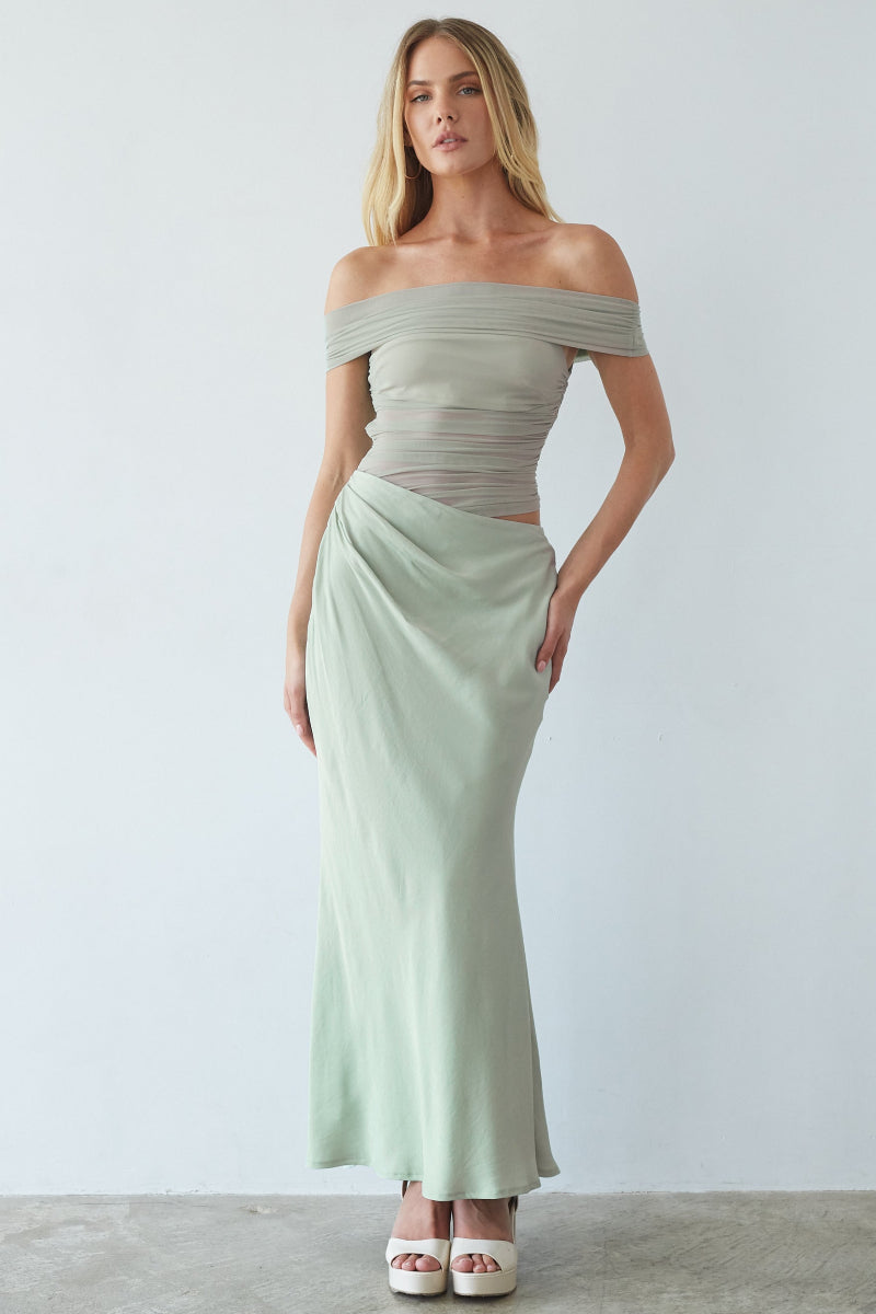 Woman wearing a light green off-shoulder top and skirt set against a white background