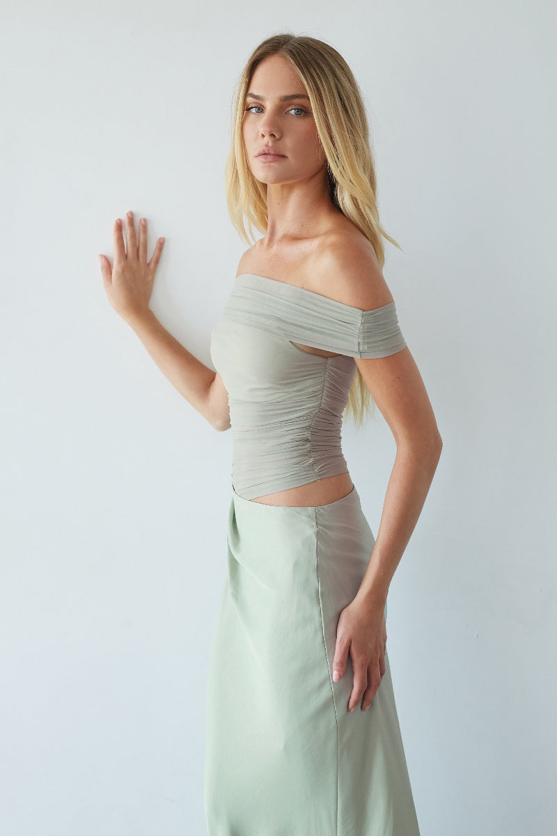 Woman wearing a gray off-shoulder top and light green skirt against a white background