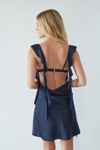 Woman wearing a navy blue dress with ruffled straps on a white background