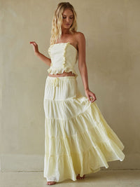 Woman wearing a light yellow strapless top and long skirt against a plain background