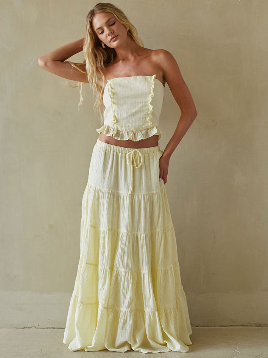 Woman wearing a light yellow strapless top and tiered skirt against a plain background