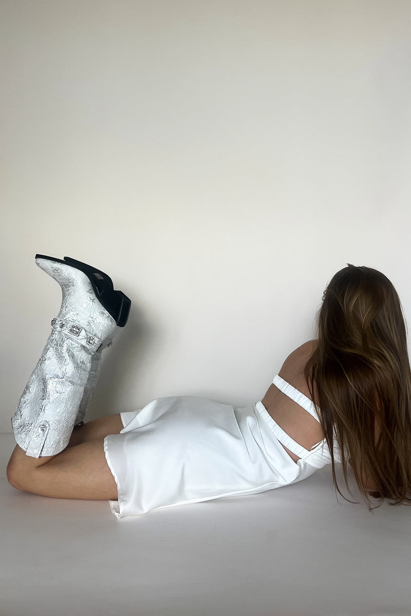 side view silver jacquard western boots - model laying face down on floor in white dress in front of white background - azalea wang trendy boutique boots