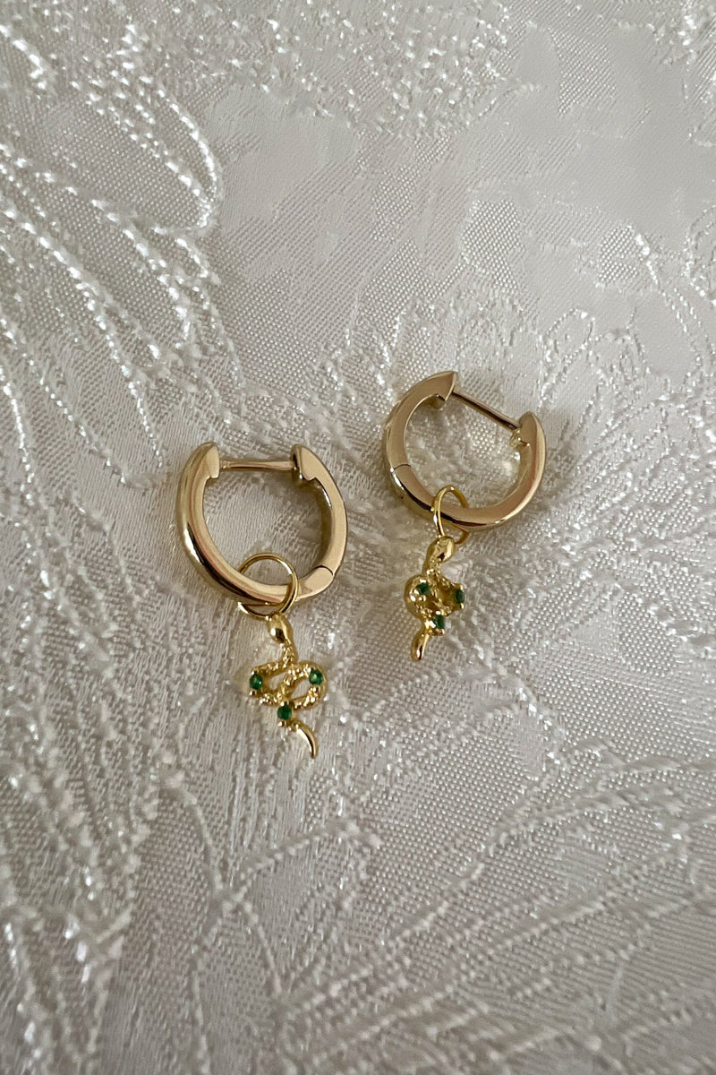 yellow gold snake charm hoop earrings with green emeralds on an ivory jacquard background
